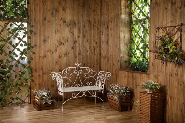 A rustic room with a wrought-iron bench, wood paneling and flowers.